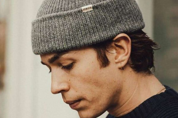 Heather grey ribbed knit beanie with small woven fabric label, worn by man in navy sweater, minimalist streetwear style
