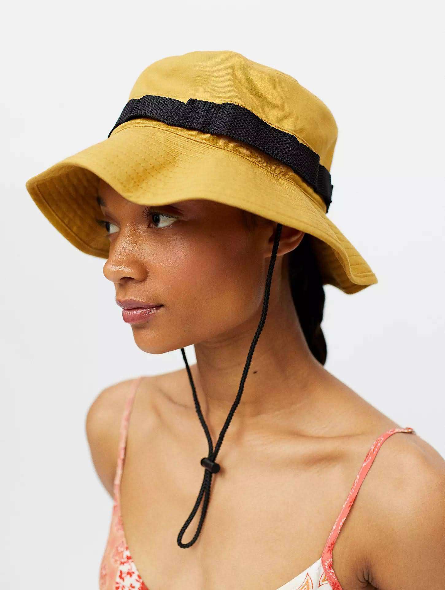 Mustard yellow utility bucket hat with black webbing strap and adjustable chin cord, outdoor adventure style