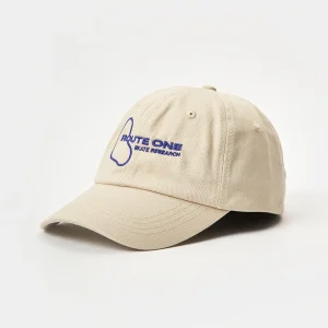 Angled front view of an unstructured beige dad hat featuring blue "Route One Skate Research" flat embroidery and a pre-curved brim.