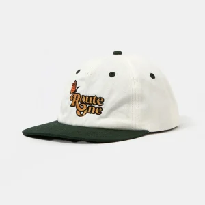 Angled front view of an unstructured off-white and forest green cotton twill 6-panel cut-and-sew dad hat featuring a flat contrasting brim and vibrant high-density multi-color "Route One" butterfly embroidery.