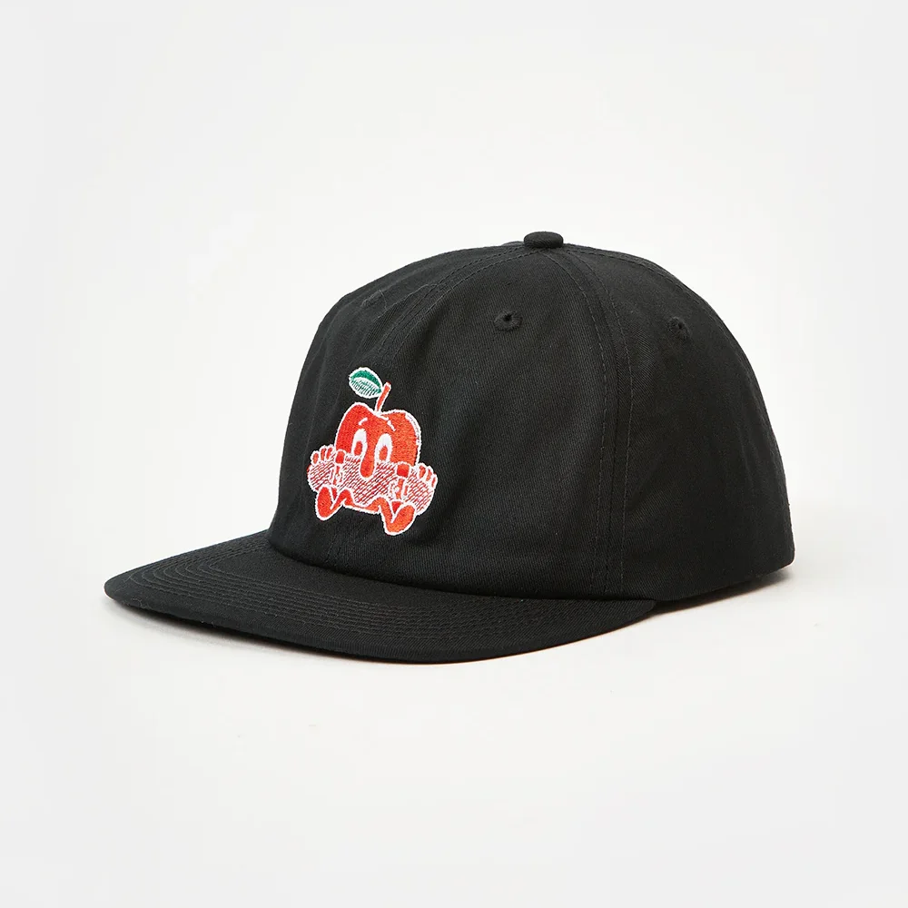 Front three-quarter view of a black unstructured cotton twill flat brim cap featuring multi-color red, white, and green cartoon apple embroidery on the front panel, with visible low-profile crown shape and flat visor angle.