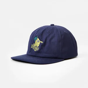 Front three-quarter view of a navy blue unstructured cotton twill flat brim cap featuring multi-color yellow, green, and white cartoon lemon embroidery on the front panel, with visible low-profile crown shape and flat visor angle.