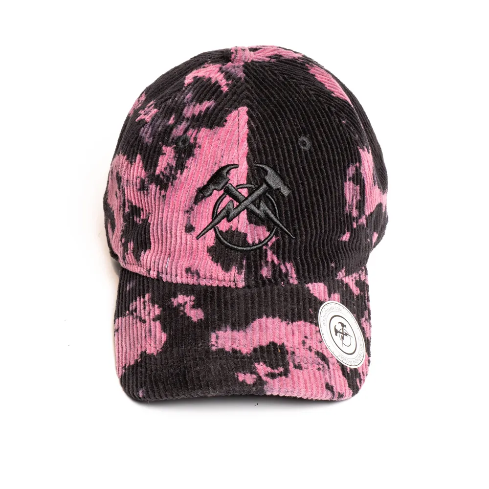 Direct front view of a pink and black tie-dye corduroy unstructured dad hat displaying centered tonal black flat embroidery across the front seam, a circular white branded sticker on the pre-curved brim, and soft low-profile crown structure.